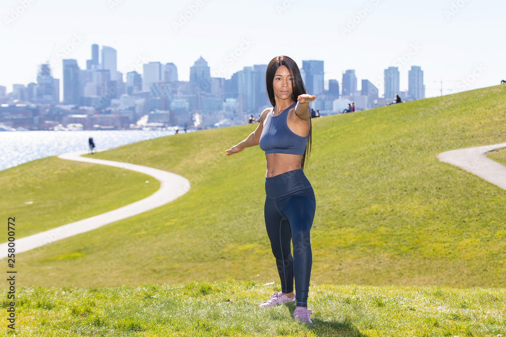 Beautiful woman with long black hair wearing yoga pants and sports bra outside during park workout