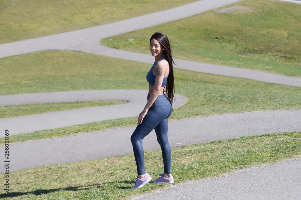 Beautiful woman with long black hair wearing yoga pants and sports bra  outside during park workout Stock Photo