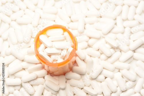 High angle view of a prescription bottled filled with pills surrounded by more of the same tablets