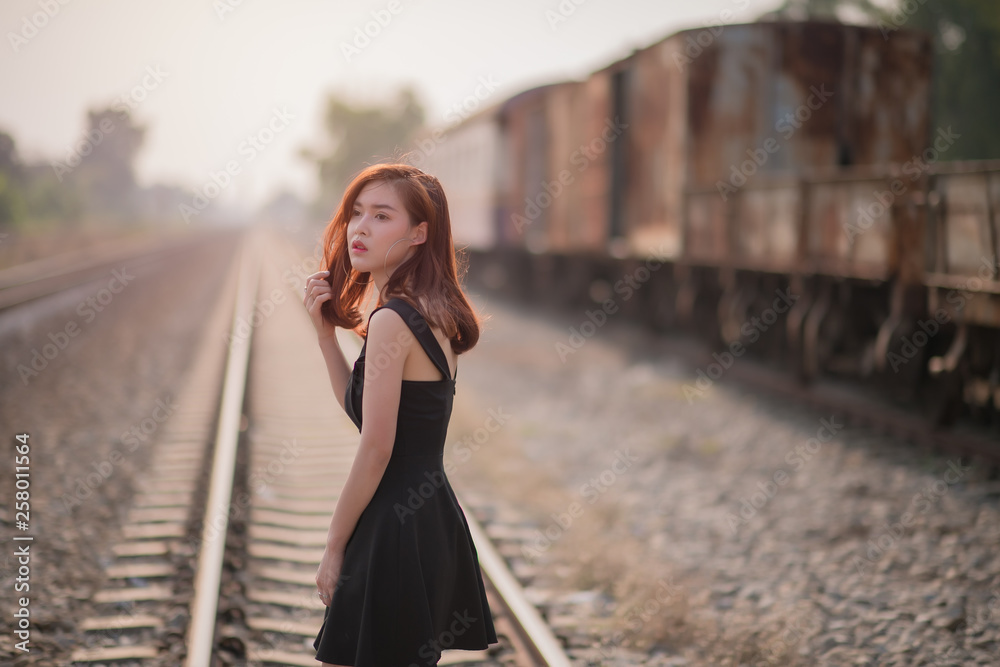 lonely young asian woman on railway track wearing black dress over train blur background.