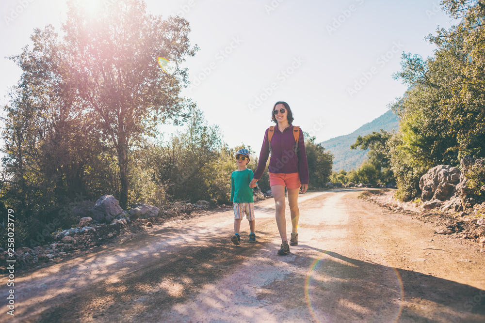 The boy walks with his mother on a mountain road.