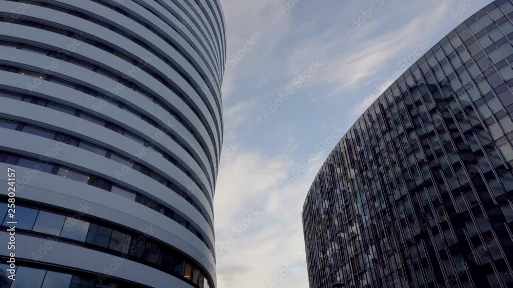 Tilt shot of glass corporate modern office buildings with visible blue sky in London. Tilt shot goes as low as street level with traffic and classic London red two deck buses. Tilt shot of glass corporate modern office buildings with visible blue sky in London. Tilt shot goes as low as street level with traffic and classic London red two deck buses.
