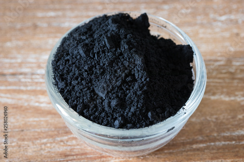Close up of activated black charcoal powder in a glass bowl on wooden background