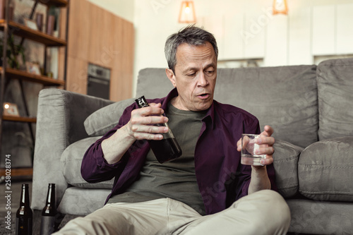 Boozy grey-haired old man sitting on floor and flooding his grief