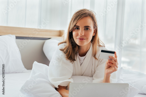 Woman with credit card on bed near laptop