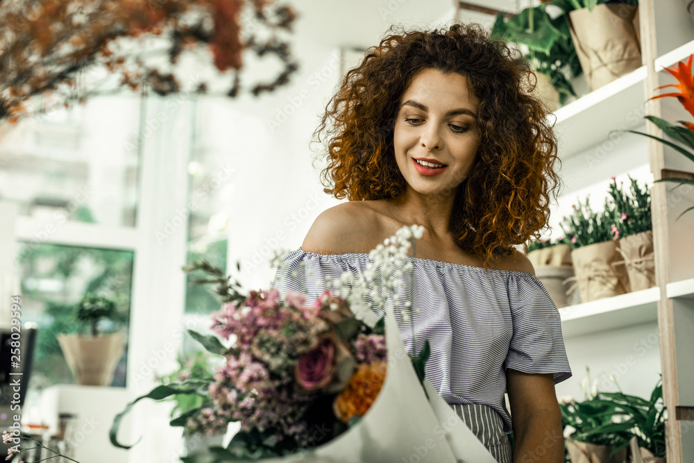 Curly florist feeling satisfied while looking at nice perfect bouquet