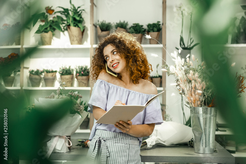 Fotografi Curly florist speaking by phone while receiving order from constant client