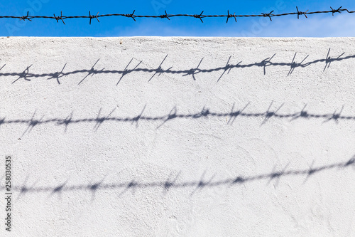 Barbed wire under blue sky with shadows