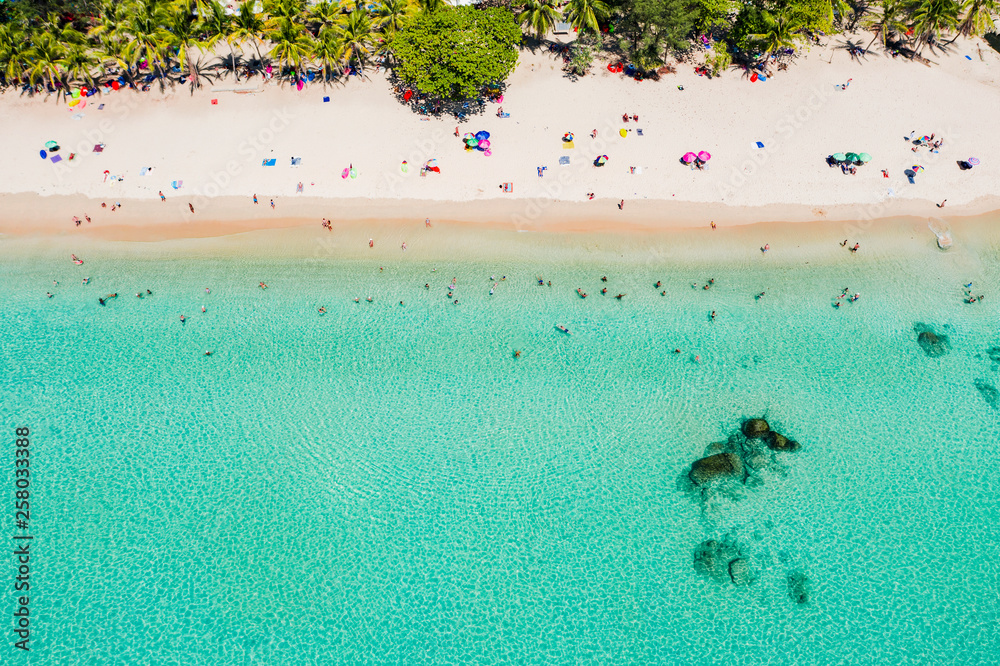View from above, stunning aerial view of  people sunbathing, swimming and relaxing on a beautiful tropical beach with white sand and turquoise clear water, Surin beach, Phuket, Thailand.