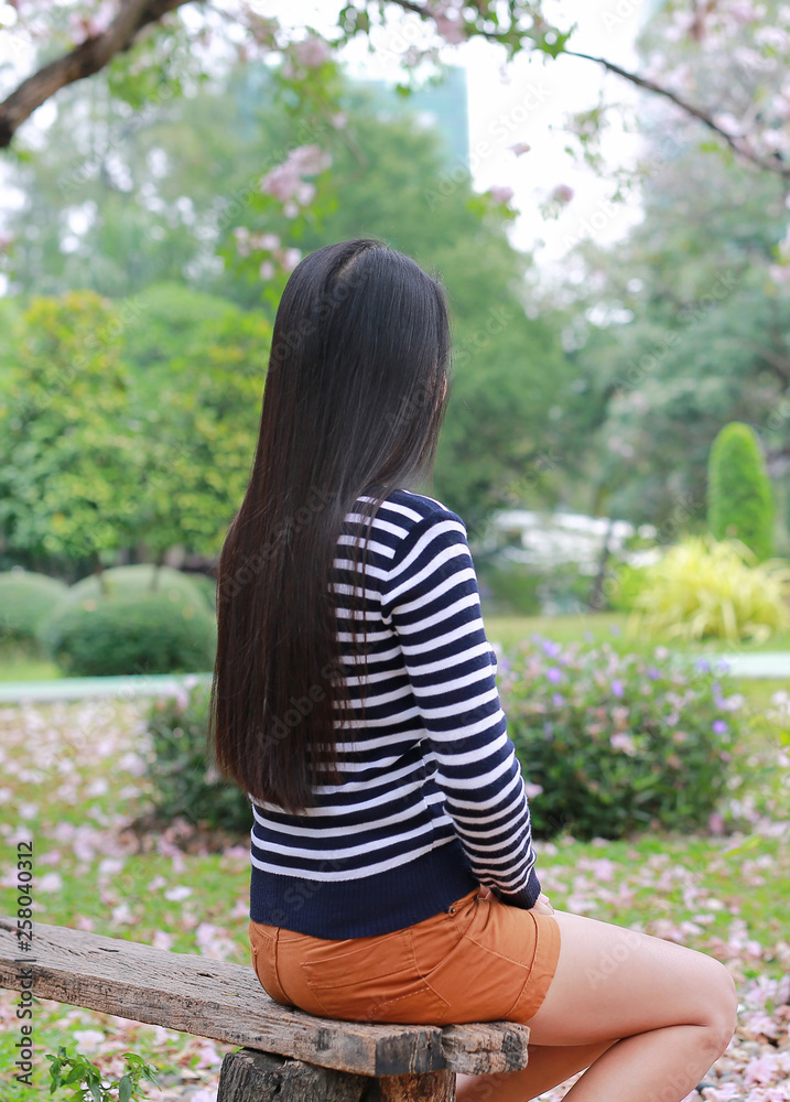 Naklejka premium Rear view Asian woman sitting on wood bench in the garden outdoor with looking out.