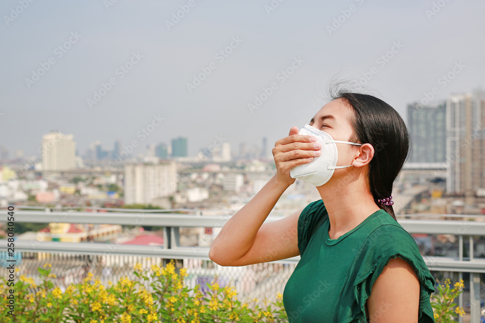 Young Asian woman wearing a protection mask against PM 2.5 air pollution in Bangkok city. Thailand. Reduce air pollution concept. Young Asian woman wearing a protection mask against PM 2.5 air pollution in Bangkok city. Thailand. Reduce air pollution concept.
