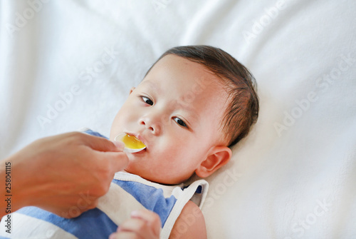 Asian baby boy takes medicine syrup from a spoon. Sick child.