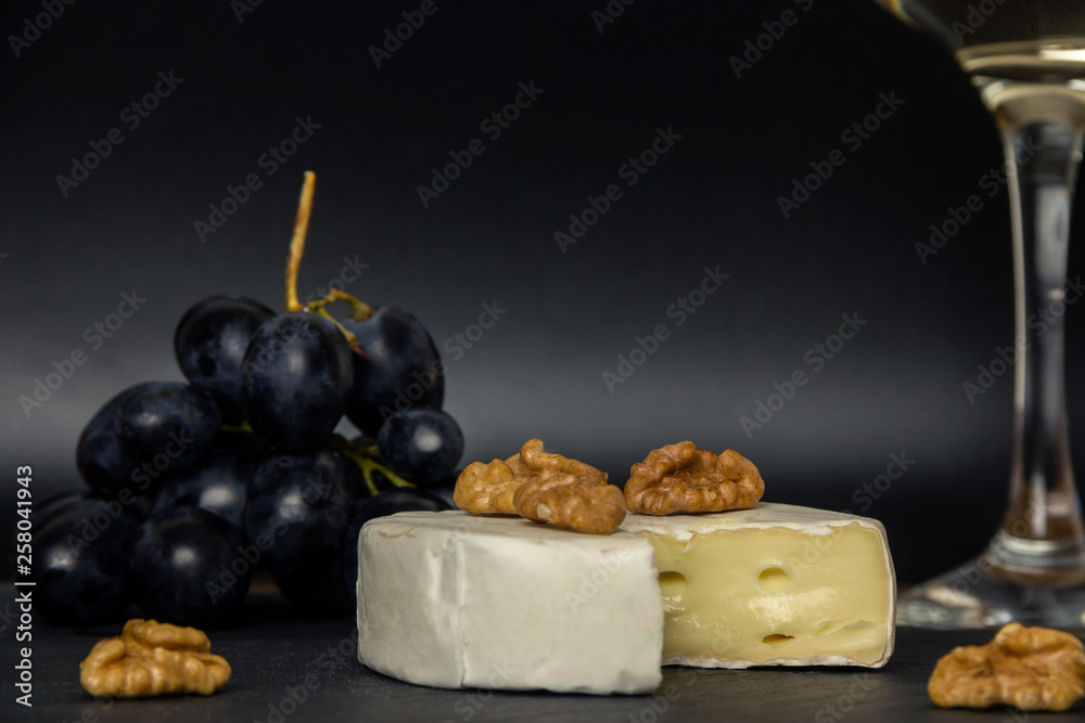 Close-up chopped camembert cheese, nuts and sweet blue grapes on the background of a glass of white dry wine
