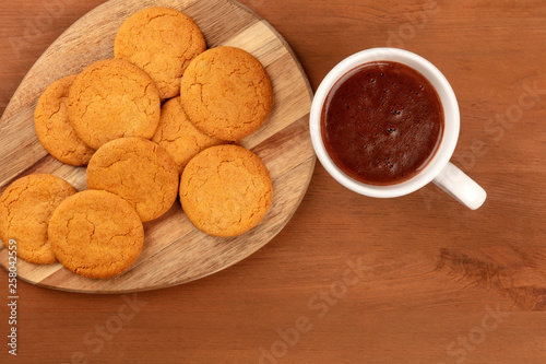 A closeup of gingersnaps, shot from the top with a cup of hot chocolate on a rustic wooden background with a place for text