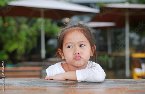 Sassy little Asian child girl with funny face lying on the wooden table. photo
