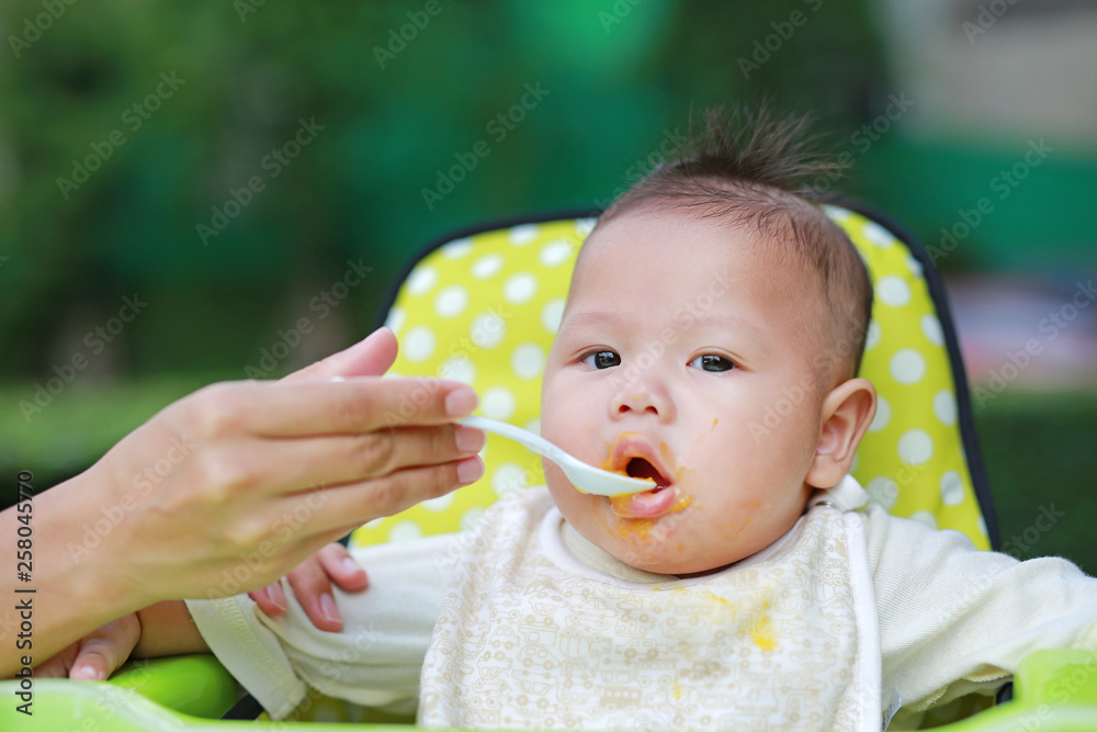 Close up infant baby boy feeding food on the kid chair in the garden. First time infant baby for feeding food. Close up infant baby boy feeding food on the kid chair in the garden. First time infant baby for feeding food.