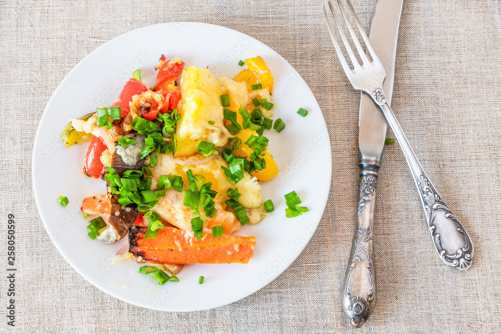Vegetables baked with cheese in a white plate on a rustic background, top view - vegetable casserole Vegetables baked with cheese in a white plate on a rustic background, top view - vegetable casserole