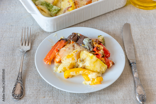 Vegetables baked with cheese in a white plate on a rustic background, top view - vegetable casserole