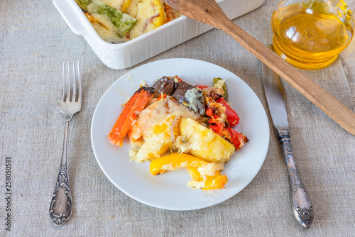 Vegetables baked with cheese in a white plate on a rustic background, top view - vegetable casserole