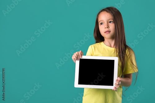 cute little child girl holding tablet with blank screen isolated on blue background