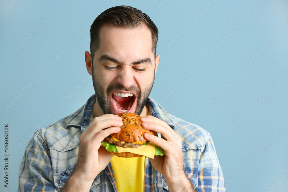 Man eating tasty burger on color background
