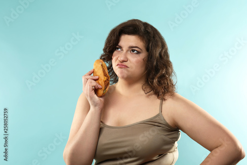 Displeased overweight woman with sandwich on color background. Weight loss concept