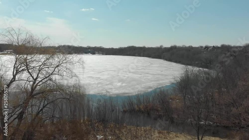 Aerial Drone video from Lake Susan in Chanhassen Minnesota flying through the trees to the receding ice melt of the lake water photo