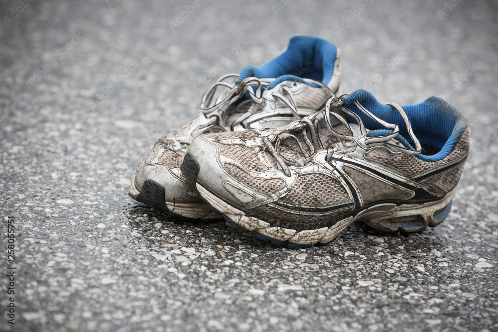 Worn, dirty, smelly and old running shoes on a tarmac road.