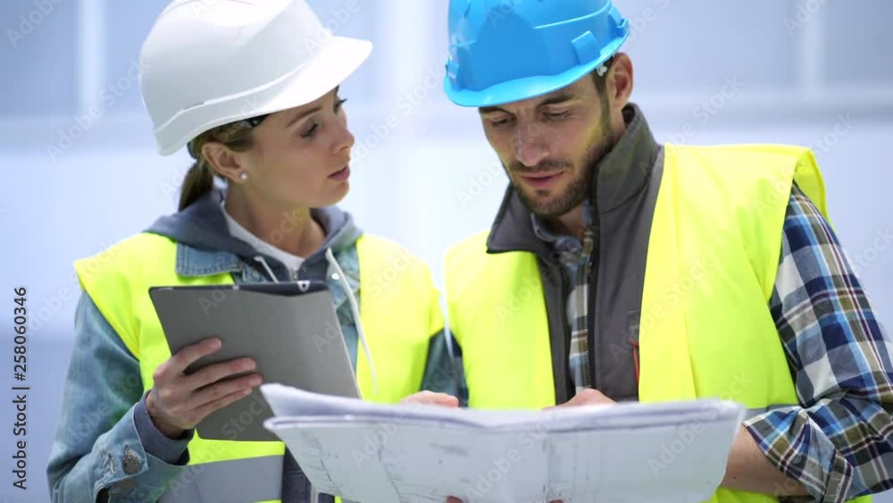 Male and female construction wokers looking over blueprint in empty warehouse Male and female construction wokers looking over blueprint in empty warehouse