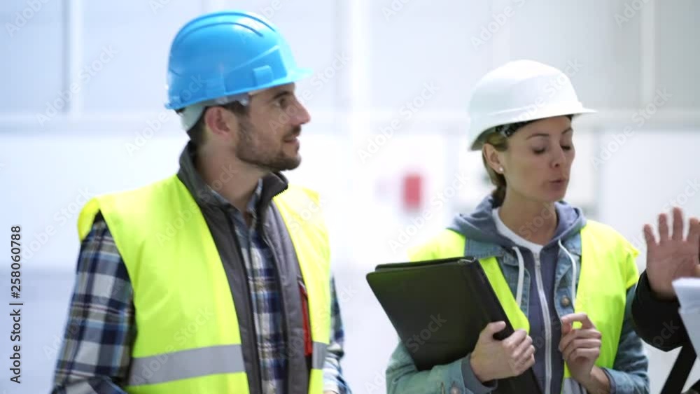 Mixed team of construction workers talking over plan in warehouse Mixed team of construction workers talking over plan in warehouse