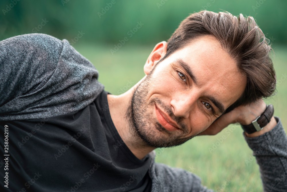 Young handsome man lying down on the green grass, enjoying a sunset relaxation in a park Young handsome man lying down on the green grass, enjoying a sunset relaxation in a park