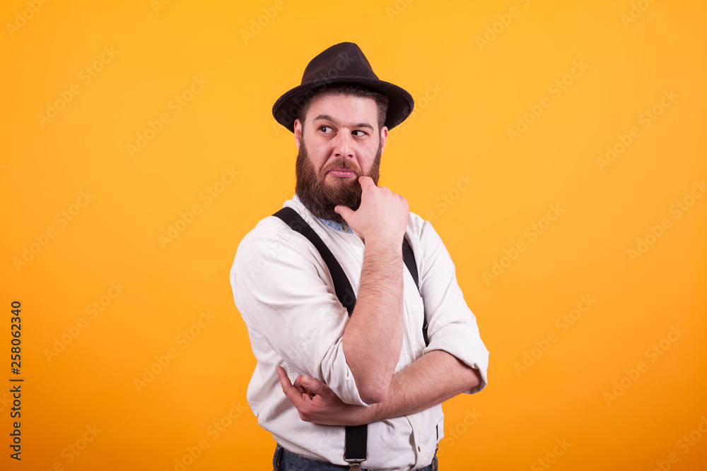 Thoughtfull bearded man with hat keeping his arms crossed over yellow background Thoughtfull bearded man with hat keeping his arms crossed over yellow background