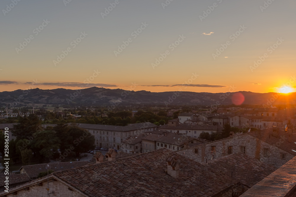 A sweeping view of the rooftops of Gubbio at sunset taken from the main Piazza Grande in the town centre with the sun dipping on the far fright of the photo