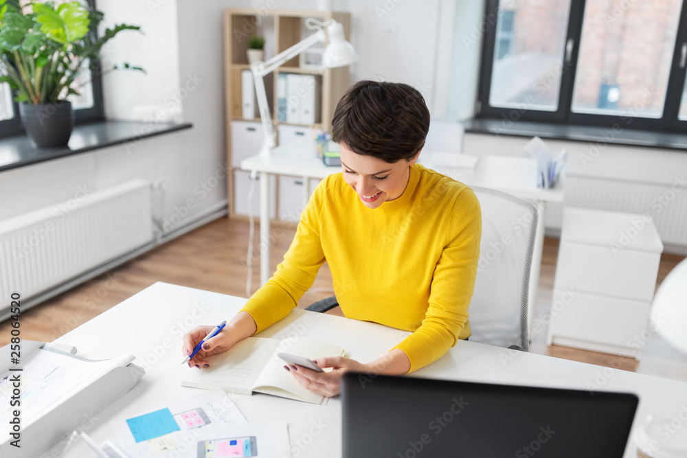 business, technology and user interface design concept - smiling ui designer with user interface templates and notebook using smartphone at office business, technology and user interface design concept - smiling ui designer with user interface templates and notebook using smartphone at office