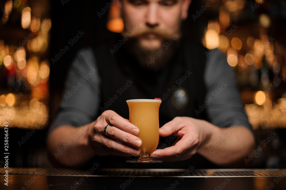 Bartender with a beard serving a cocktail in the glass with foam decorated with a one red rose bud Bartender with a beard serving a cocktail in the glass with foam decorated with a one red rose bud