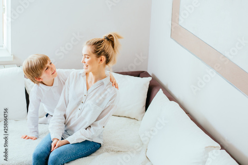 Portrait of cute blond mother anb kid are hugging, laughing, playing together in cozy home. They are holding each other with joy while relaxing on sofa. photo