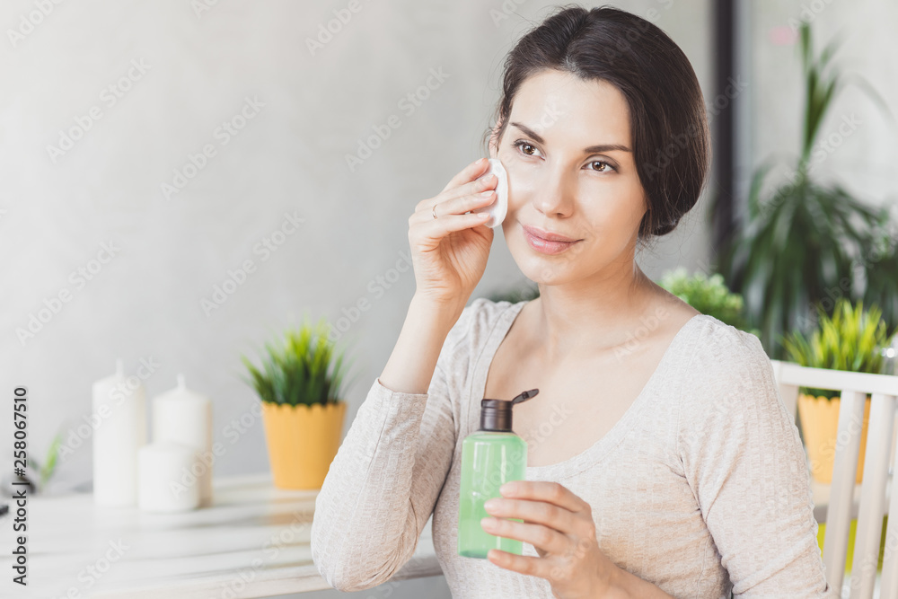 Makeup remove skin care. Closeup woman holding cotton swab and makeup remover liquid cosmetic in hands. Woman cleaning her face with lotion and cotton pad Makeup remove skin care. Closeup woman holding cotton swab and makeup remover liquid cosmetic in hands. Woman cleaning her face with lotion and cotton pad