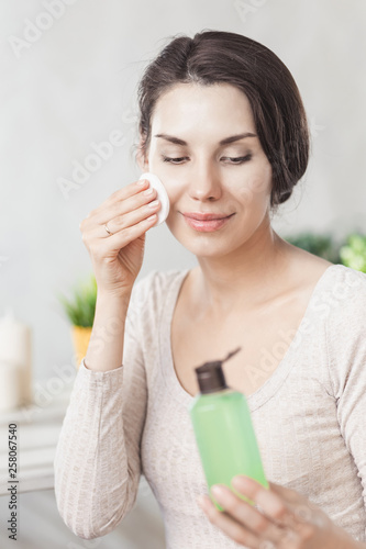 Makeup remove skin care. Closeup woman holding cotton swab and makeup remover liquid cosmetic in hands. Woman cleaning her face with lotion and cotton pad