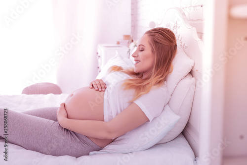 Young long-haired pregnant woman in a white t-shirt touching her belly