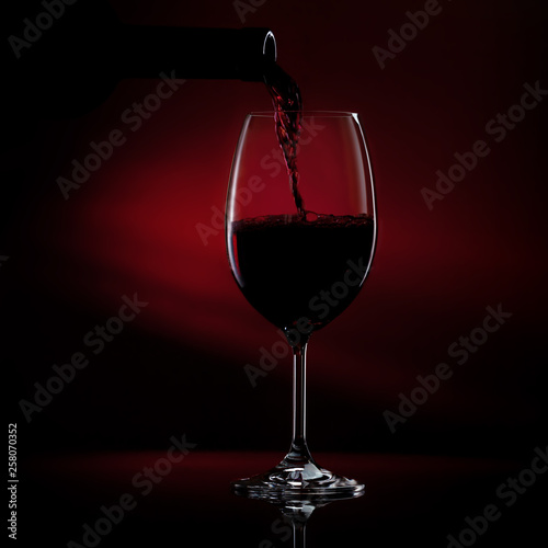 Pouring red wine from a bottle into a wine glass on a black background. Close-up studio shot.