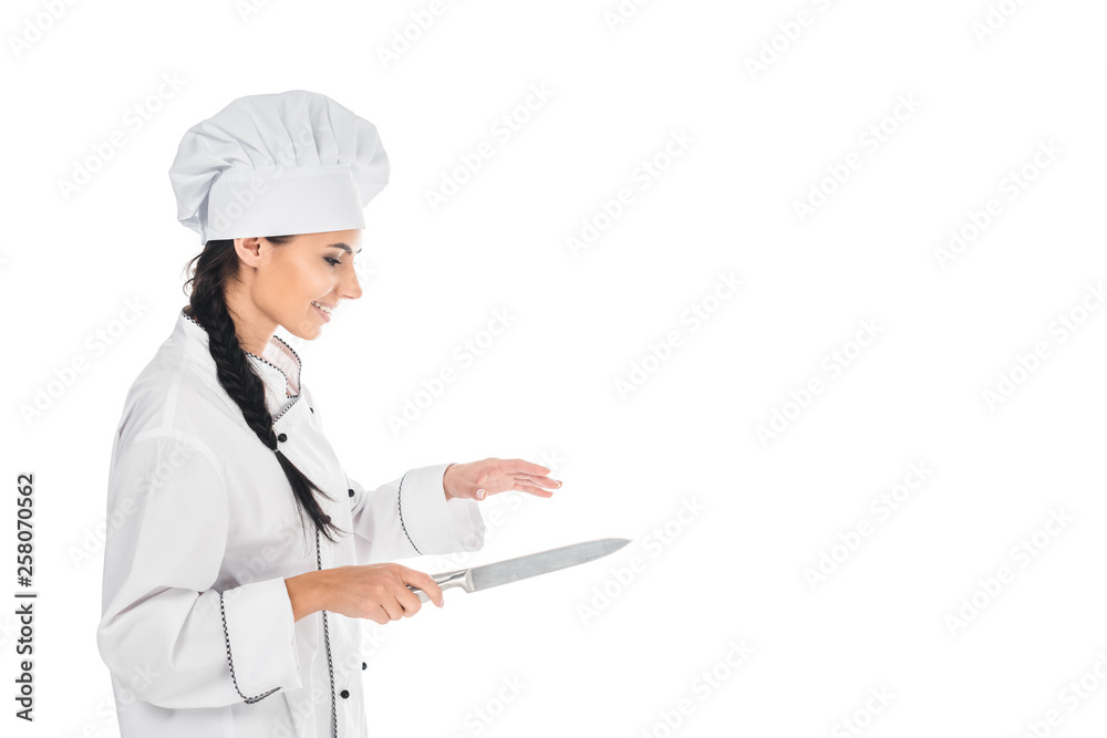 Side view of smiling chef in uniform holding knife isolated on white Side view of smiling chef in uniform holding knife isolated on white