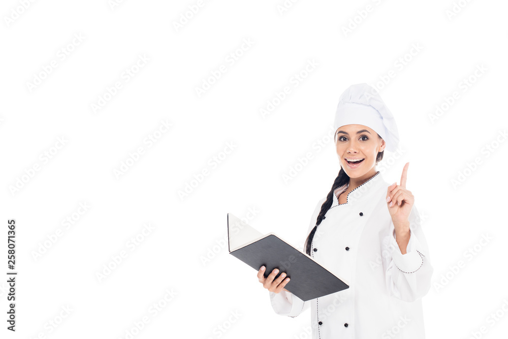 Amazed chef in uniform holding black book and showing idea gesture isolated on white
