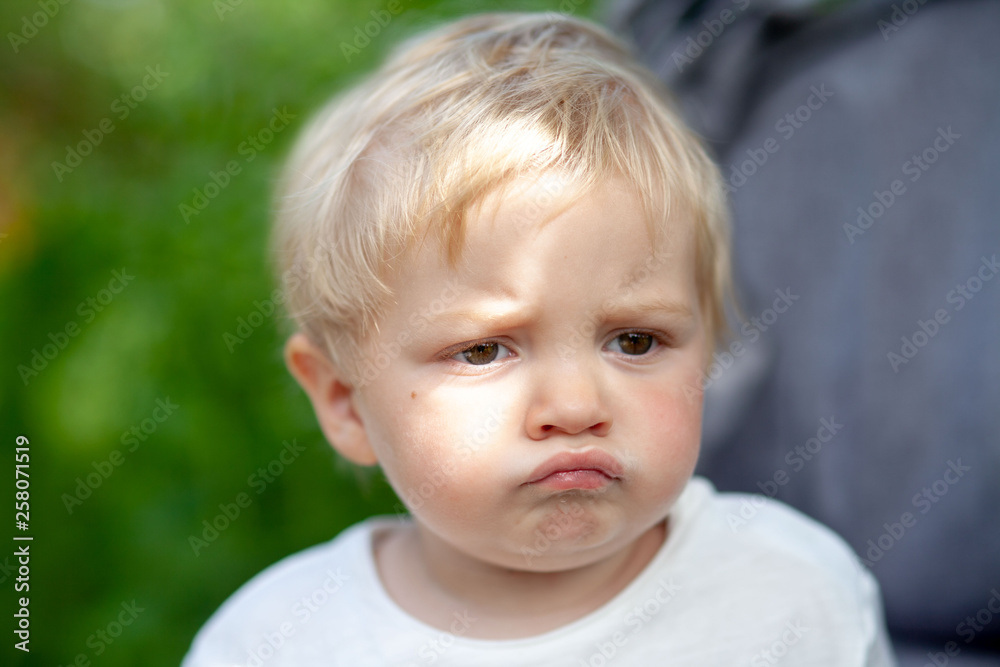 Emotional little boy portrait in the park with green trees on background Emotional little boy portrait in the park with green trees on background
