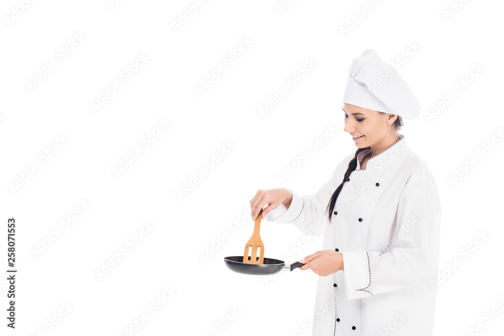 Chef in hat holding frying pan and wooden kitchen spatula isolated on white Chef in hat holding frying pan and wooden kitchen spatula isolated on white