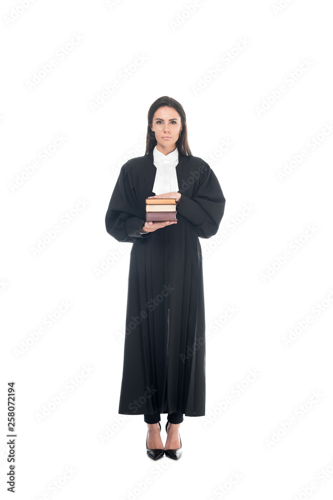 Full length view of serious judge in judicial robe holding books isolated on white Full length view of serious judge in judicial robe holding books isolated on white