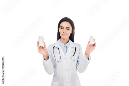 Doctor in white coat with stethoscope holding pills isolated on white