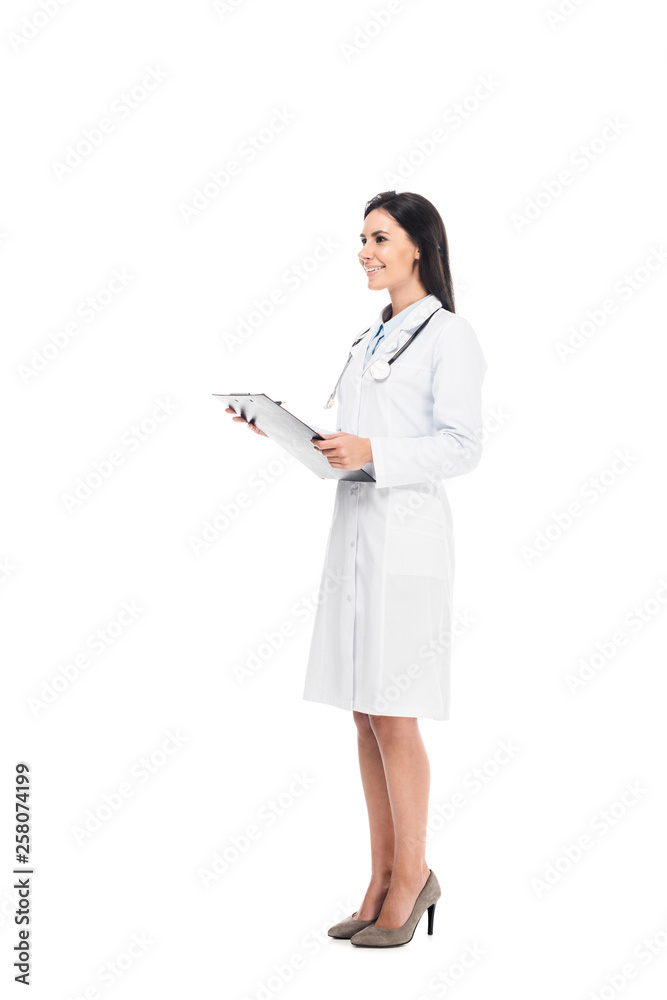 Full length of smiling doctor in white coat holding clipboard isolated on white Full length of smiling doctor in white coat holding clipboard isolated on white