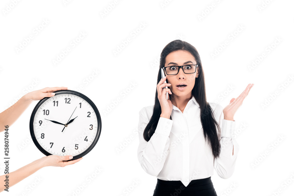 Shocked businesswoman talking on smartphone near clock isolated on white Shocked businesswoman talking on smartphone near clock isolated on white