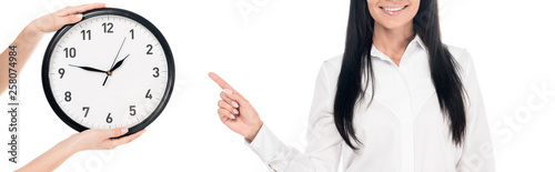 Panoramic shot of smiling businesswoman in glasses pointing with finger at clock isolated on white