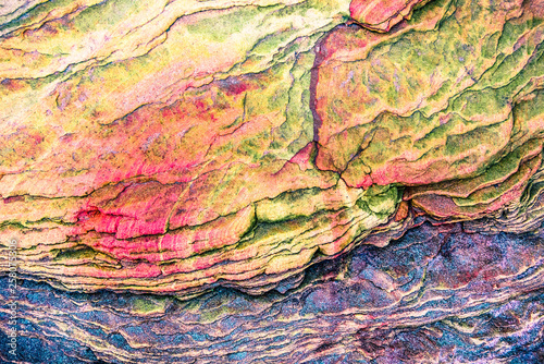 Multicolored rock wall from bottom sediments red orange dark rays crack smooth